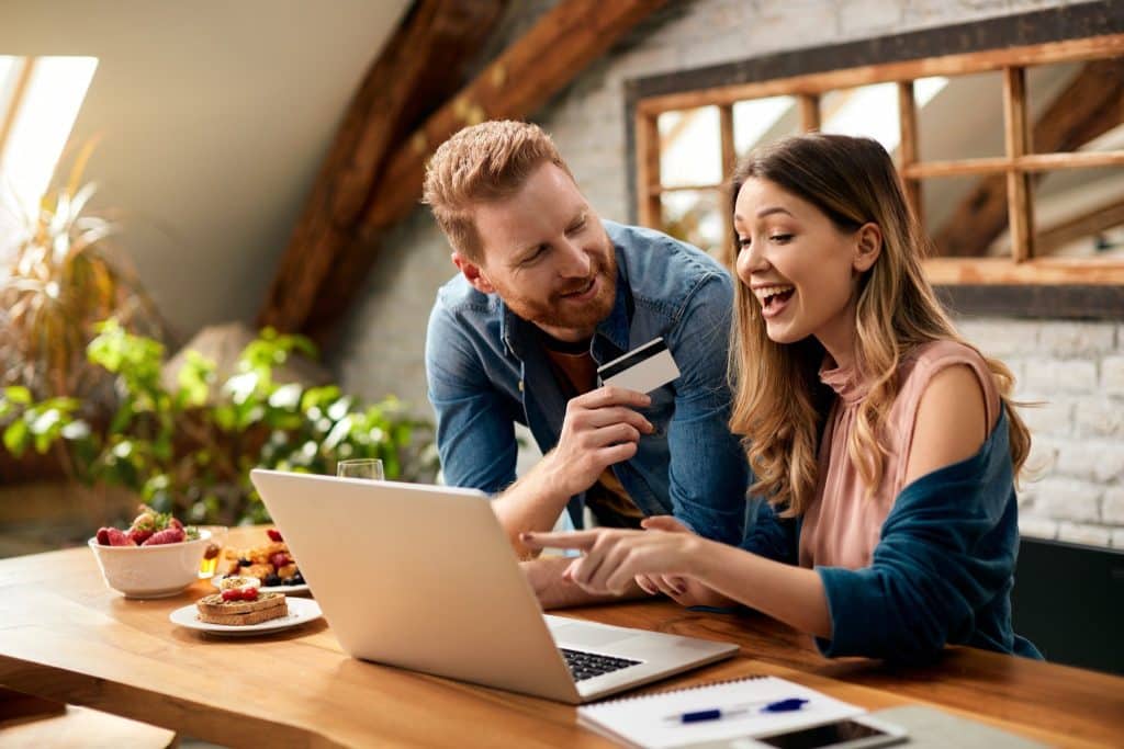 Excited couple using a credit card while budgeting online, illustrating managing monthly finances together.