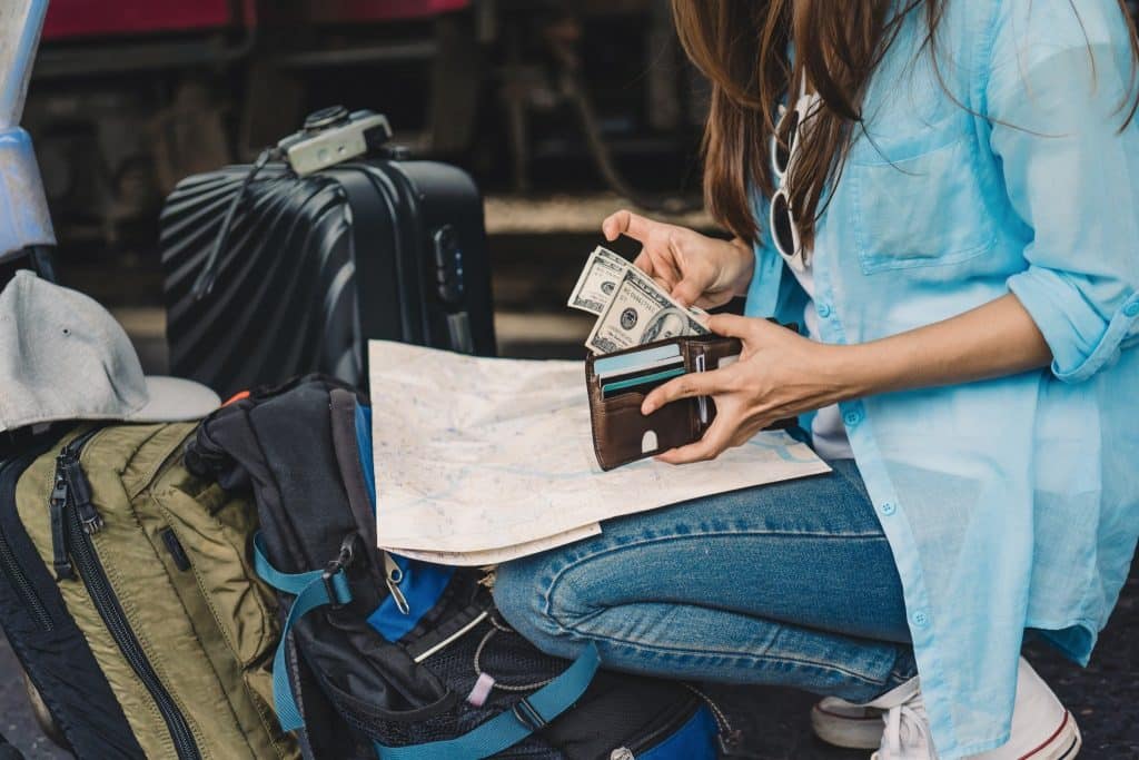 Traveler checking wallet with dollar bills and map, planning to travel on a budget