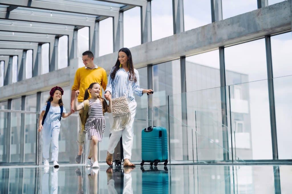 Parents and children walking together through an airport with luggage, capturing budget family travel tips for smart flying.