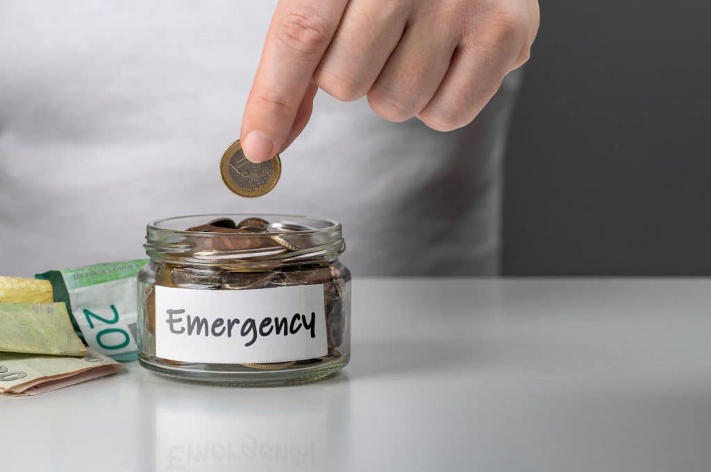 Hand dropping a coin into a jar labeled emergency, showing the act of building emergency fund savings.