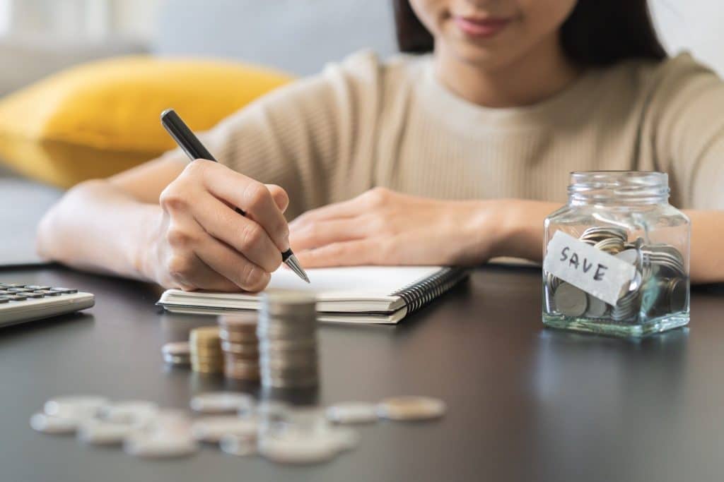 Person writing financial plans with a savings jar, showing gratitude and money mindset.