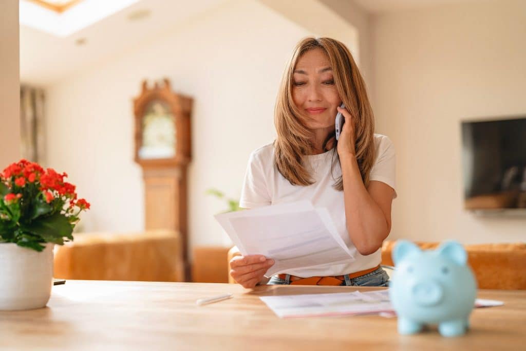 Woman on phone holding bills with piggy bank, representing gratitude and money habits.