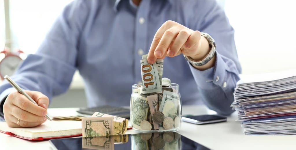 Person saving money in a jar while writing a budget plan — holiday spending tips for smarter shopping.