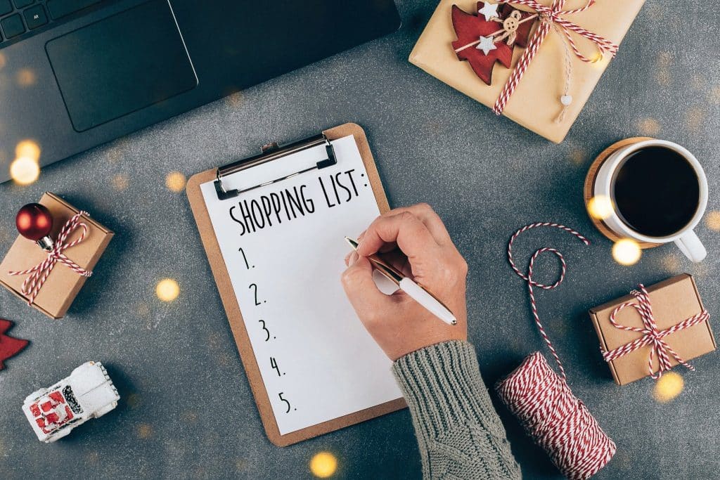 Holiday shopping list on clipboard with gifts and coffee — holiday spending tips to plan purchases in advance.