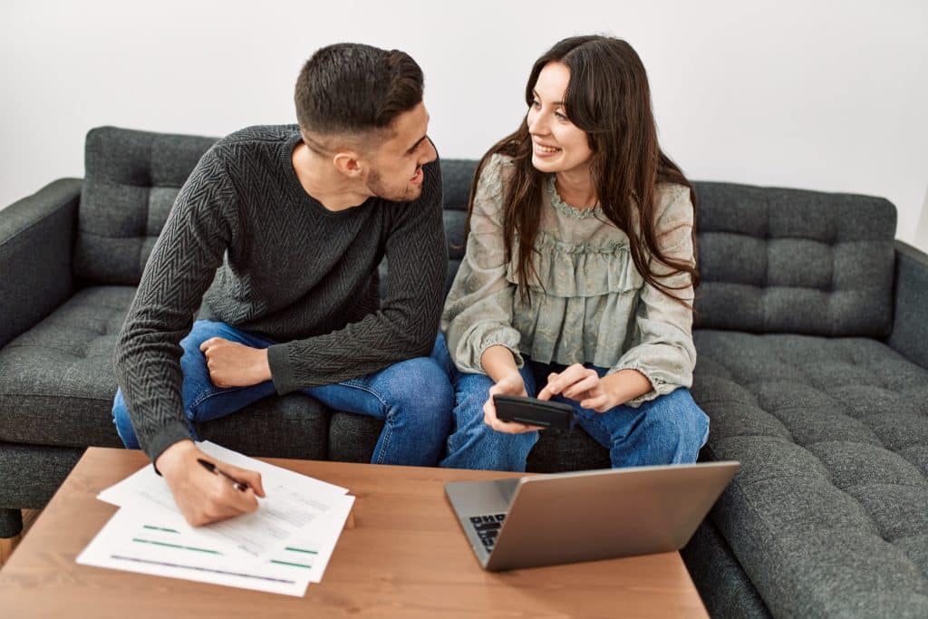 Couple budgeting together on a couch with a laptop, working on overcoming money stress as a team.