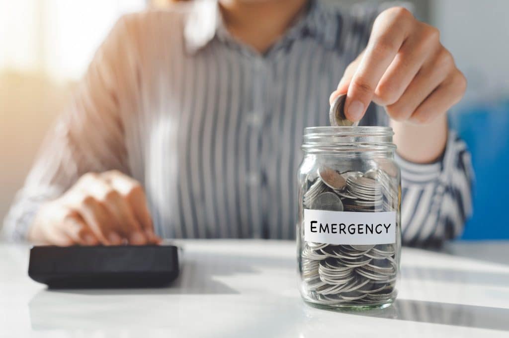 Person adding coins to an emergency savings jar, showing a proactive step in overcoming money stress. 