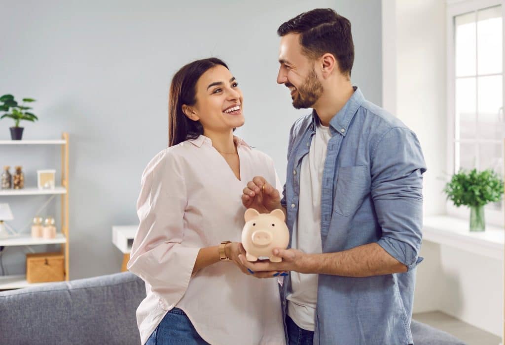 Couple holding a piggy bank, smiling while applying realistic financial advice for future savings.
