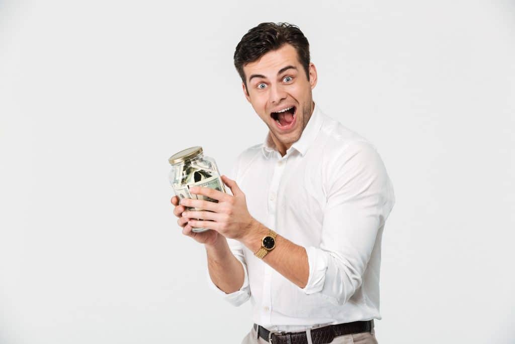 A happy individual holding a jar full of rolled bills, highlighting the excitement of managing and saving money to reduce monthly expenses.