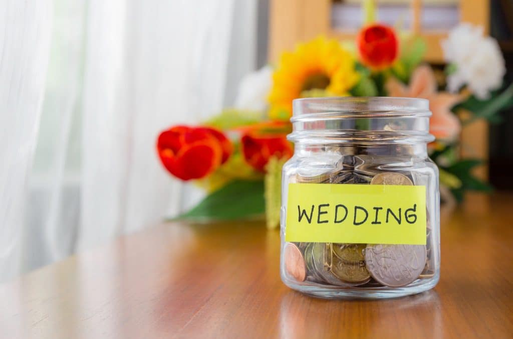 A glass jar labeled wedding filled with coins and savings, reflecting how wedding budgeting tips help couples set a practical budget from the start.