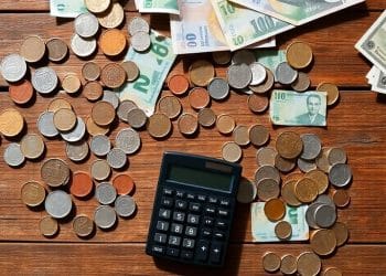Coins, bills, and a calculator on a wooden table.