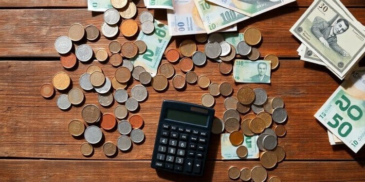 Coins, bills, and a calculator on a wooden table.