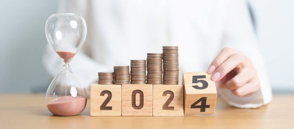 Stacked coins with changing year blocks and hourglass, representing the long-term impact of generational saving on financial wellness.