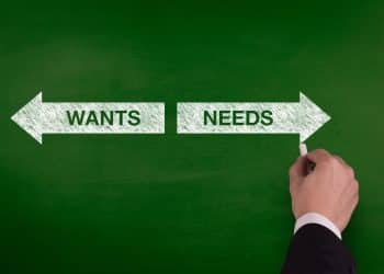 Arrow sign pointing to wants and needs on a chalkboard, symbolizing choices in managing monthly finances.