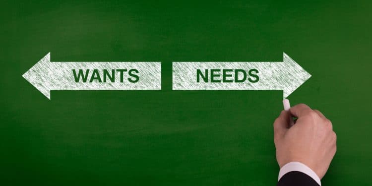 Arrow sign pointing to wants and needs on a chalkboard, symbolizing choices in managing monthly finances.