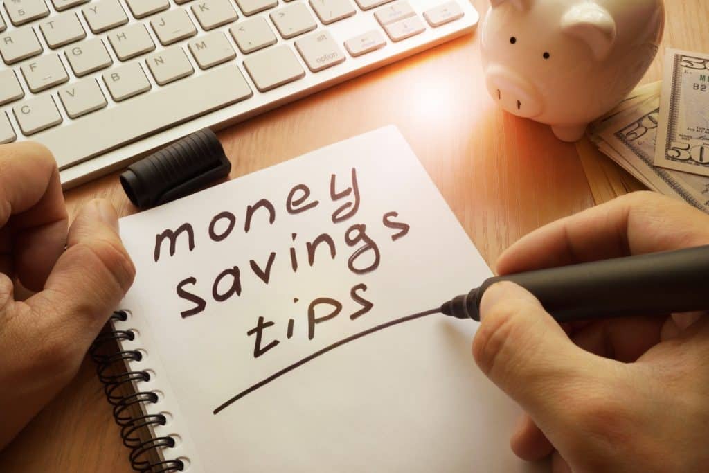 Writing down tips to save money in a notebook beside a piggy bank and cash—practical reminder to prioritize personal budgeting.