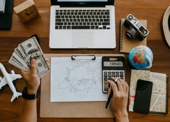 Flat lay of travel essentials, calculator, and money for planning to travel on a budget