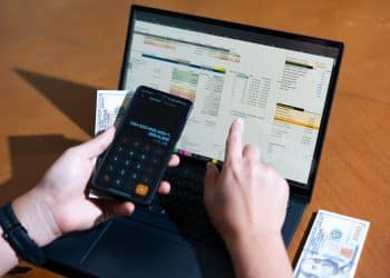 A person using a calculator and laptop to track expenses, showing how the best budgeting apps 2025 help organize finances right from the start.