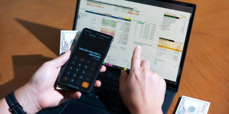 A person using a calculator and laptop to track expenses, showing how the best budgeting apps 2025 help organize finances right from the start.