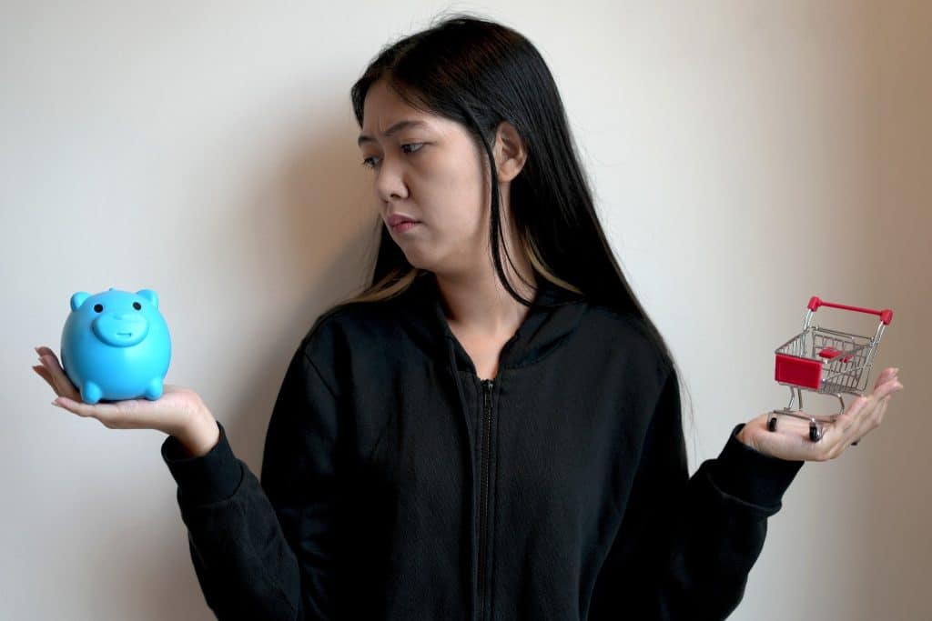 Woman deciding between saving in a piggy bank and shopping, showing the struggle of breaking bad money habits.