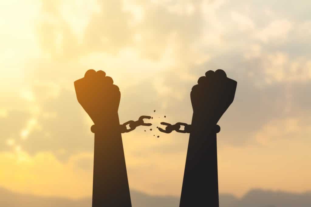 Silhouette of hands breaking free from chains at sunrise, symbolizing breaking bad money habits and financial freedom.