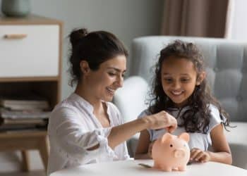 Mother helping her daughter save coins in a piggy bank, a positive step toward breaking bad money habits and learning financial discipline.