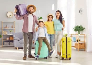Family with kids happily packing suitcases at home, showing budget family travel tips in action before starting their trip.