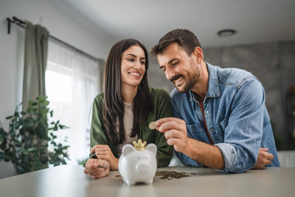 Happy couple saving coins in a piggy bank to build healthy money habits.