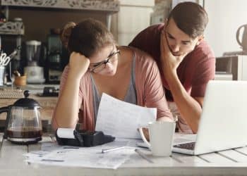 Couple stressed over bills at kitchen table while managing monthly budget.