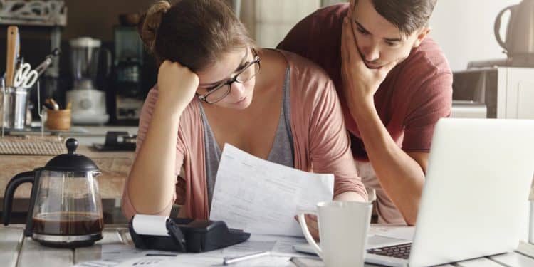 Couple stressed over bills at kitchen table while managing monthly budget.