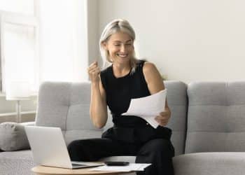 Smiling woman reviewing bills on a laptop, showing success in overcoming money stress.