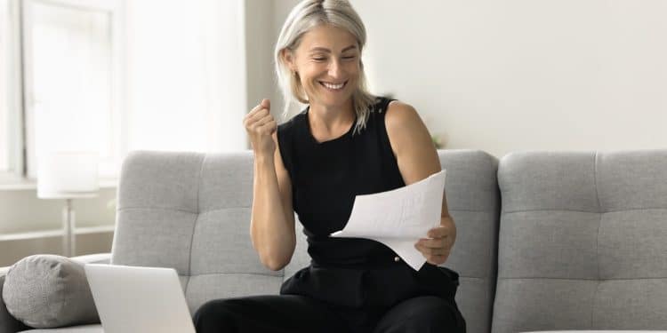 Smiling woman reviewing bills on a laptop, showing success in overcoming money stress.