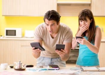 Couple reacting to unexpected expenses while budgeting at home, highlighting the need for realistic financial advice.