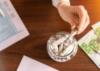 Image showing a person placing rolled banknotes into a jar, emphasizing the importance of saving money to reduce monthly expenses like cutting subscriptions.