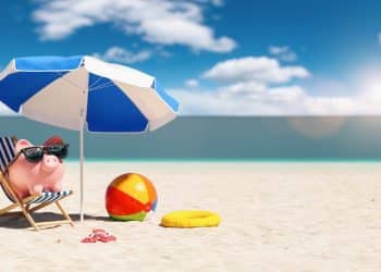 Piggy bank relaxing on a beach chair – travel budget tips for saving money on vacations.