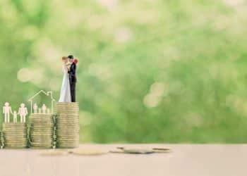 A couple standing on stacked coins symbolizes visualization for financial success and life goals like home, family, and car.
