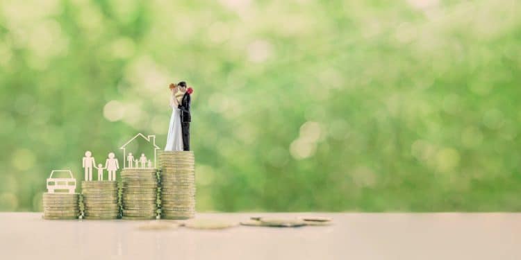 A couple standing on stacked coins symbolizes visualization for financial success and life goals like home, family, and car.