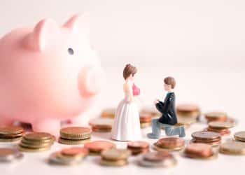 A toy couple planning their wedding expenses with coins and a piggy bank, showing the importance of wedding budgeting tips for a debt free celebration.